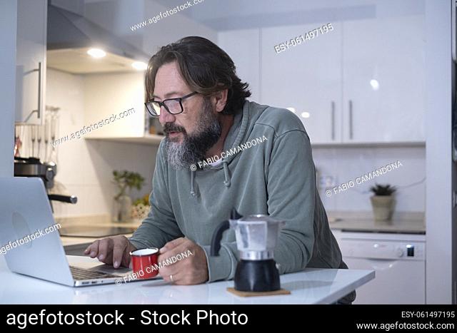 One man at home having breakfast before work drinking italian coffee. Modern people using computer laptop in the kitchen in house real lifestyle leisure