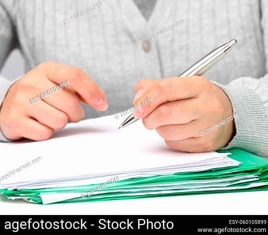 woman of Caucasian appearance sits in gray clothes at a white table and signs documents with a metal pen. Businessman at work, signature on contract and invoice