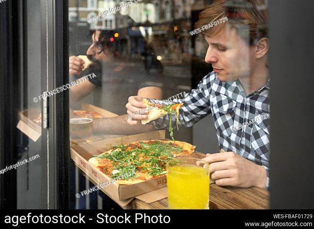 Businessman holding pizza slice while sitting at table in office