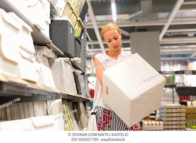 Beautiful young caucasian woman choosing the right item for her apartment in a modern home decor furnishings store. Shopping in retail store