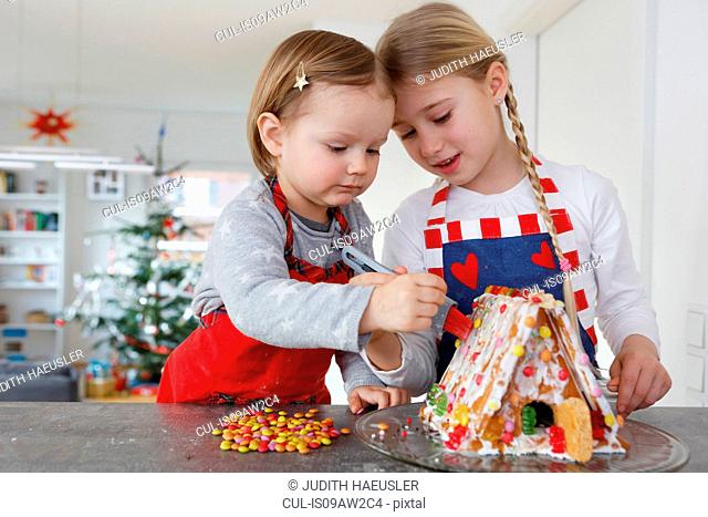 Girls at kitchen counter decorating gingerbread house together
