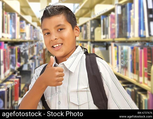 Handsome hispanic student boy with back pack and thumbs up in the library