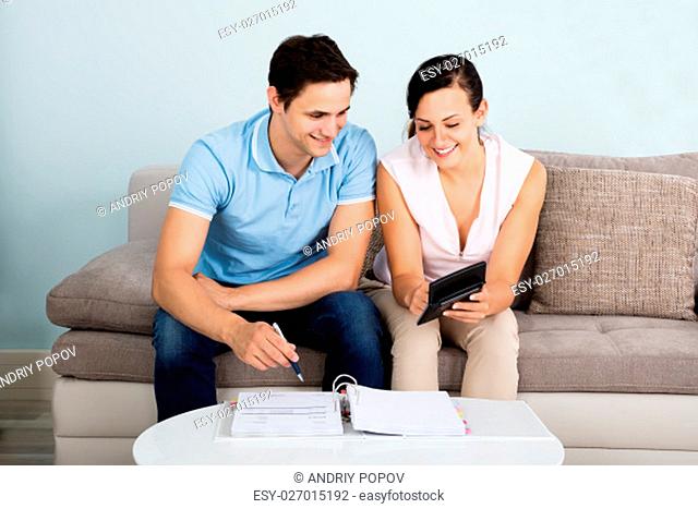 Young Happy Couple Sitting On Sofa Calculating Budget At Home