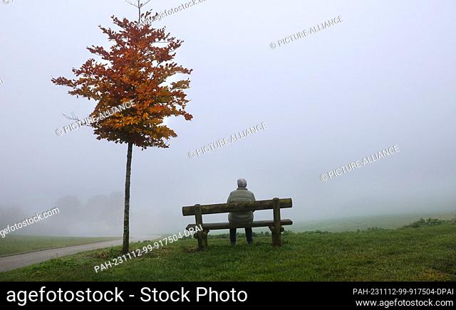 12 November 2023, Baden-Württemberg, Uttenweiler: A woman sits on a bench at a viewpoint in the fog. Photo: Thomas Warnack/dpa