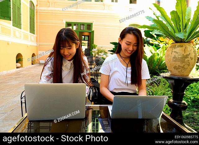 Portrait of two young beautiful Korean women together relaxing at the coffee shop outdoors