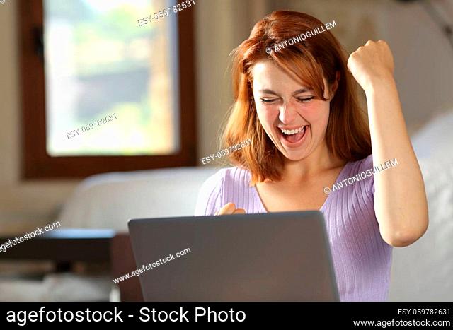 Excited woman checking laptop celebrating success in a bedroom at home