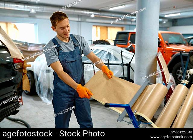 Car repair service workman taking wrapping paper to protect vehicle body from incorrect painting