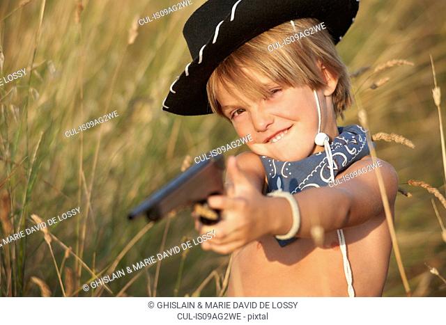 Portrait of boy in cowboy hat pointing toy gun
