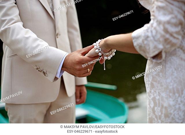 The groom gently holds the bride by the hand, close-up