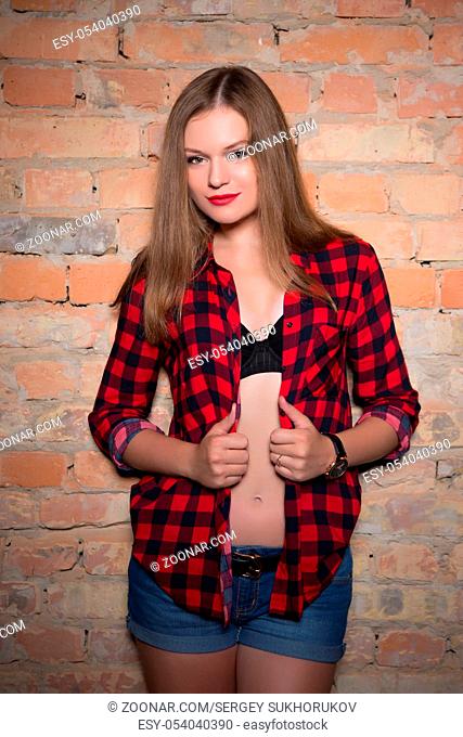 Young playful blond woman posing in checkered shirt near the wall