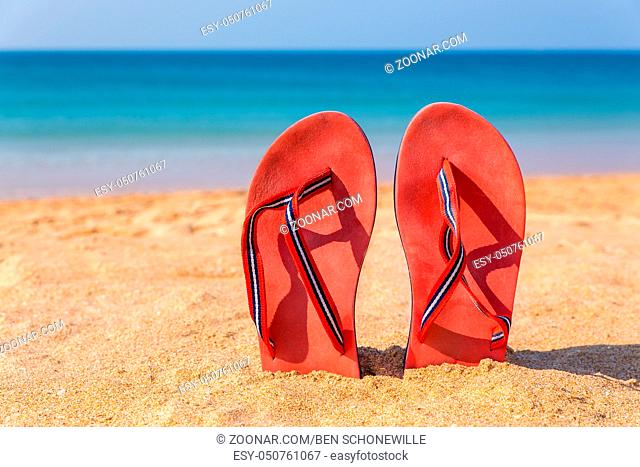 Two red bathslippers upright on beach with sea water