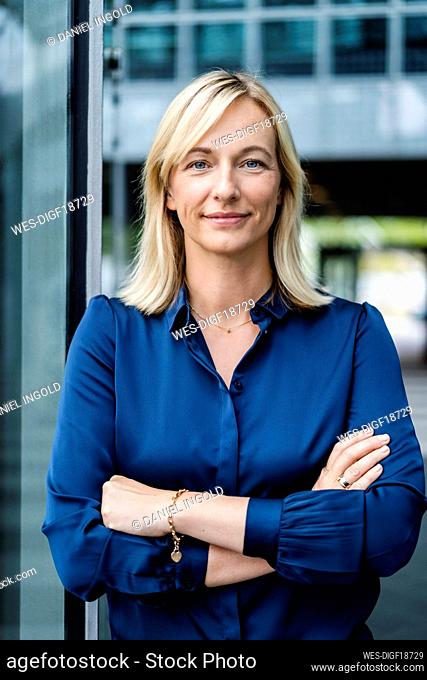 Smiling mature businesswoman with arms crossed by glass wall