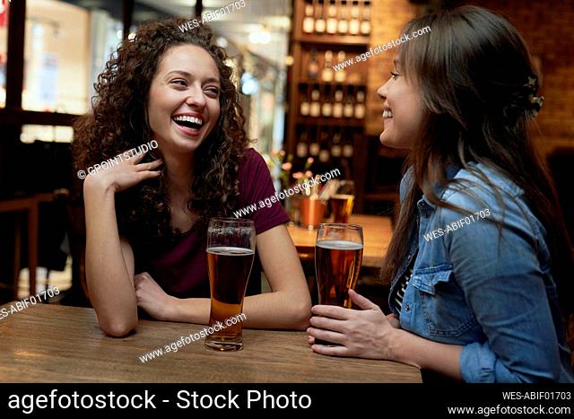 Two happy female friends having beer and socializing in a pub