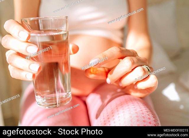 Expectant woman holding pill and drinking water on sunny day