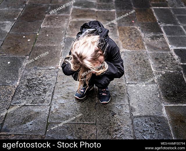 Sad lost girl crying while crouching on footpath during rainy season