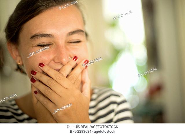 Portrait of young woman covering her mouth with hand, smiling, happy and joy