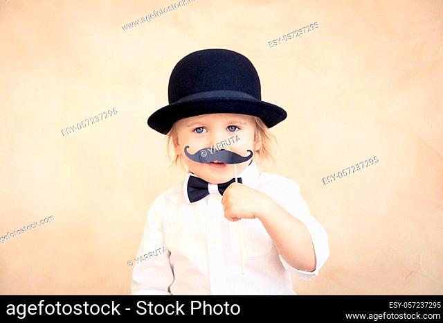 Funny kid with fake paper moustache. Happy child playing in home. Father's day concept