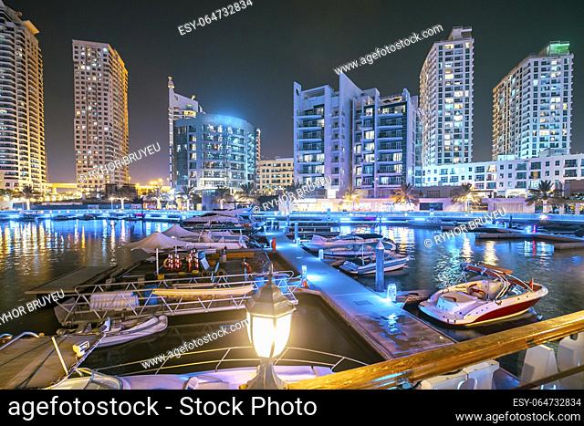 Dubai Marina Port, UAE, United Arab Emirates - Night view of high-rise buildings of residential district in Dubai Marina And Yachts Moored Near Pier In Evening...