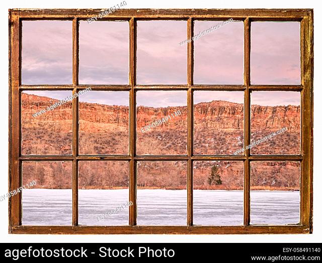 Calm dusk over Colorado foothills with frozen lake and sandstone cliff as seen from a sash window of vintage cabin