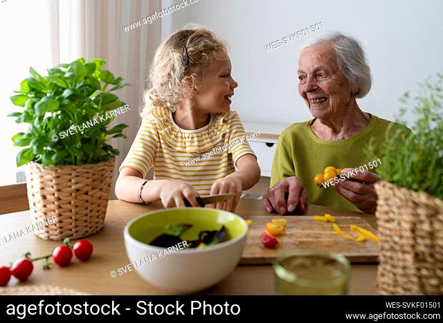 Smiling grandmother and granddaughter holding vegetable on table