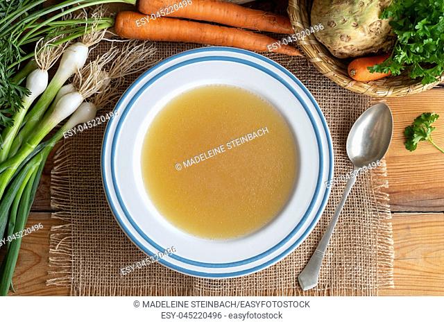 Chicken bone broth in a plate with vegetables, top view