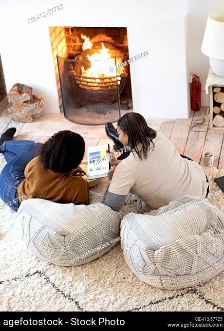 Mother and daughter using digital tablet by living room fireplace