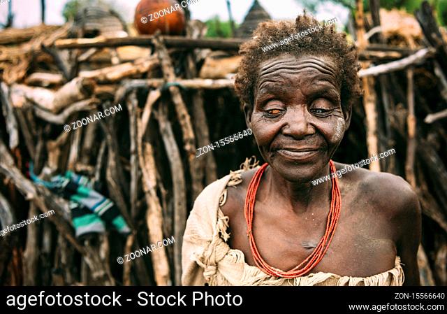 Old blind woman from Toposa Tribe standing on blurred background of stick hut in village in South Sudan, Africa