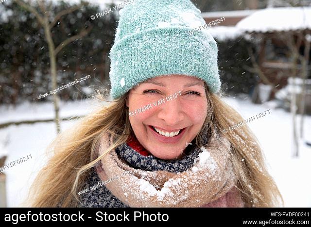 Cheerful blond woman wearing knit hat and scarf standing at backyard