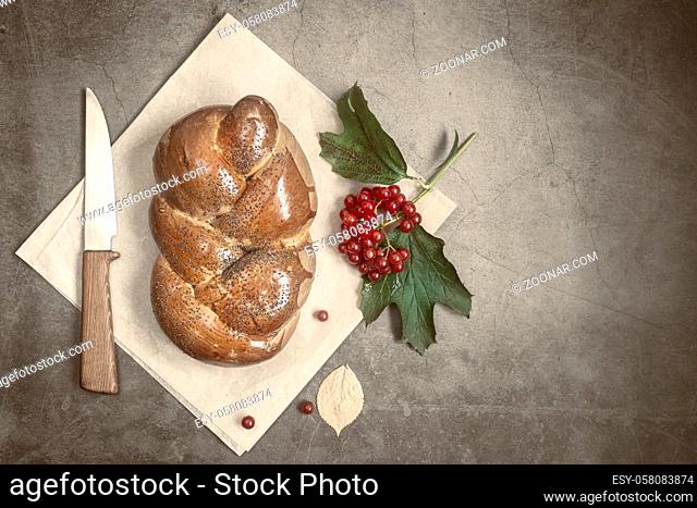 On a linen napkin is a loaf of white bread in the form of a pigtail with poppy seeds and crispy crust and a knife. Presented on a dark background, top view