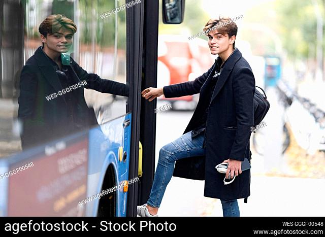 Handsome young man with backpack boarding bus in city
