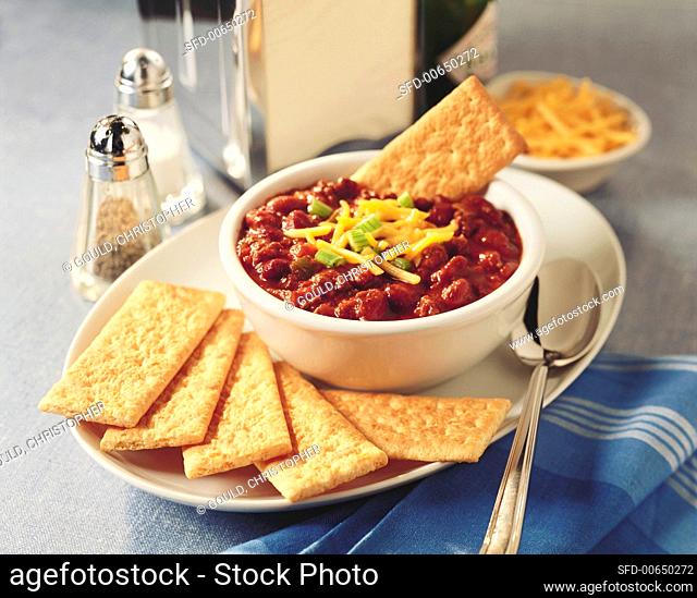 A bowl of chili with cheese and crackers