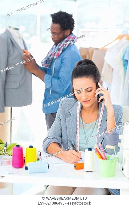 Attractive fashion designer calling while her colleague adjusting blazer on a mannequin