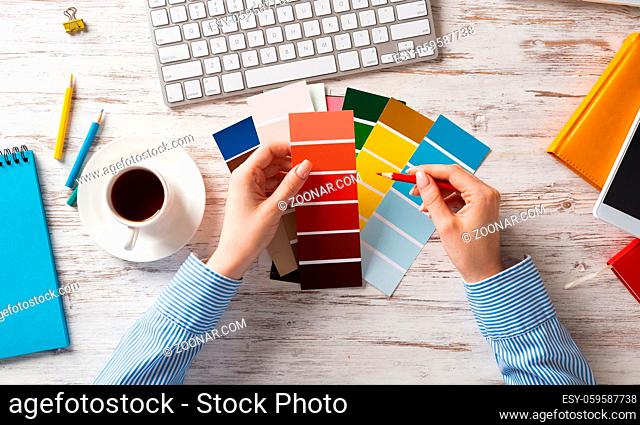 Web designer choosing colors from swatches at wooden desk. Office workplace with computer keyboard and cup of coffee. Designing user interface of mobile...