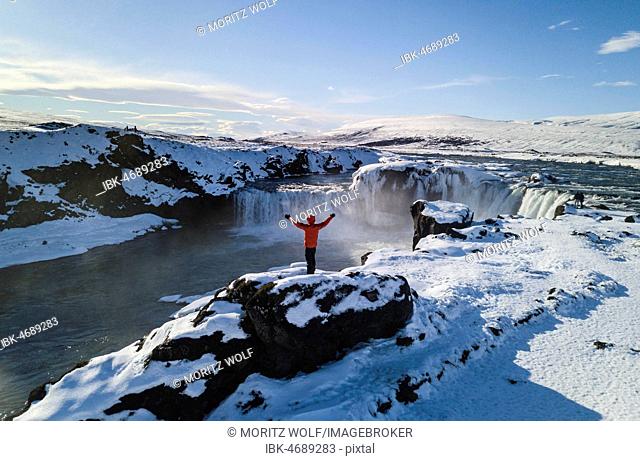 Aerial view, man standing in front of waterfall Góðafoss, Godafoss in winter with snow and ice, Norðurland vestra, North Iceland, Iceland