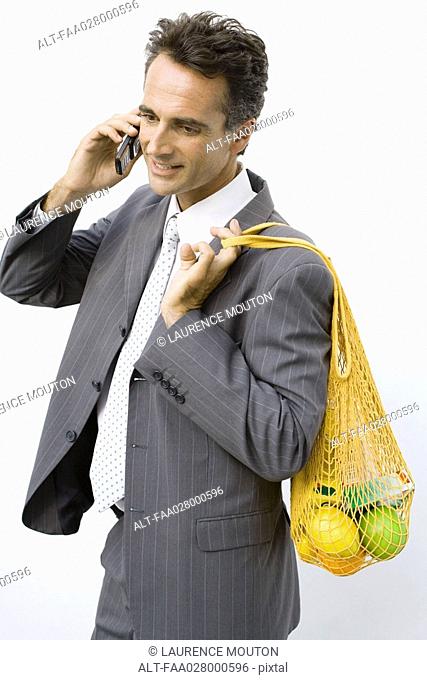 Businessman holding reusable grocery bag over shoulder, using cell phone