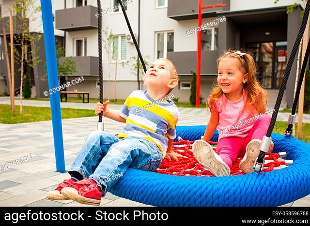 Cute little children on swing at modern playground in front of apartment building