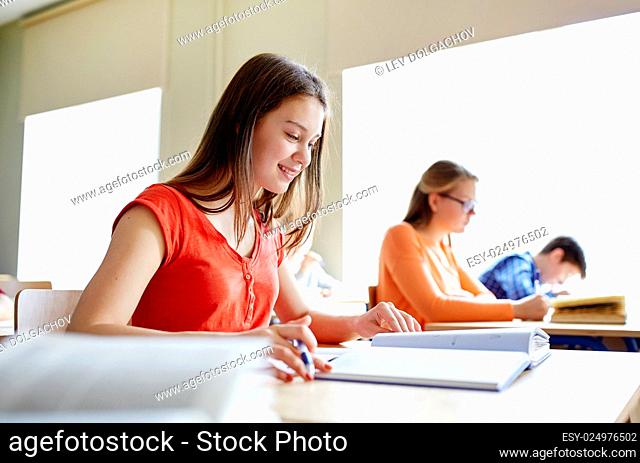 education, learning and people concept - happy student girl with book writing school test
