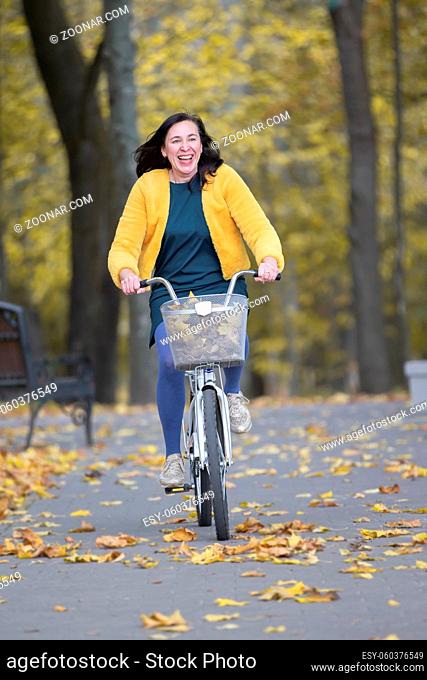 Happy middle aged woman rides a bicycle in the autumn park