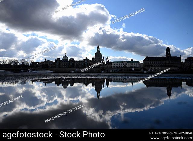 dpatop - 05 March 2021, Saxony, Dresden: The silhouette of the old town with the Frauenkirche is reflected in a puddle on the banks of the Elbe