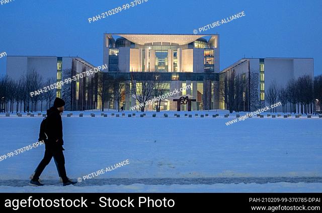 09 February 2021, Berlin: Two people walk past the Federal Chancellery at dusk. Chancellor Merkel and the state premiers are meeting this Wednesday to discuss...