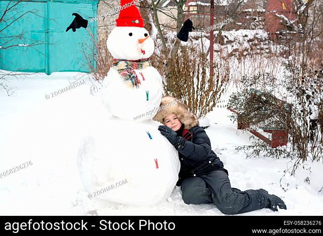 The boy in a fur hat near snowman