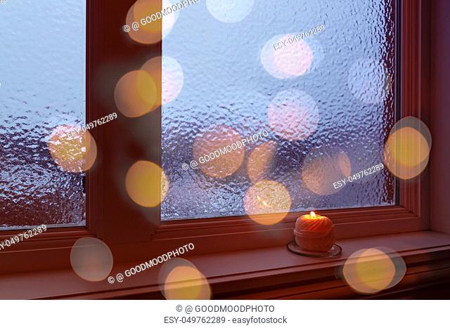 Cozy winter composition with burning candle and bokeh lights