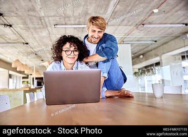 Smiling curly haired woman using laptop by boyfriend at loft