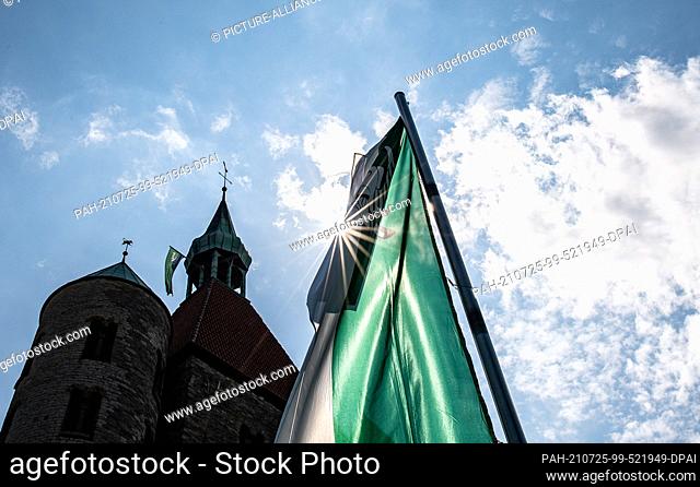 25 July 2021, North Rhine-Westphalia, Warendorf: The sun shines through a green and white marksmen's flag, hanging in front of the collegiate church