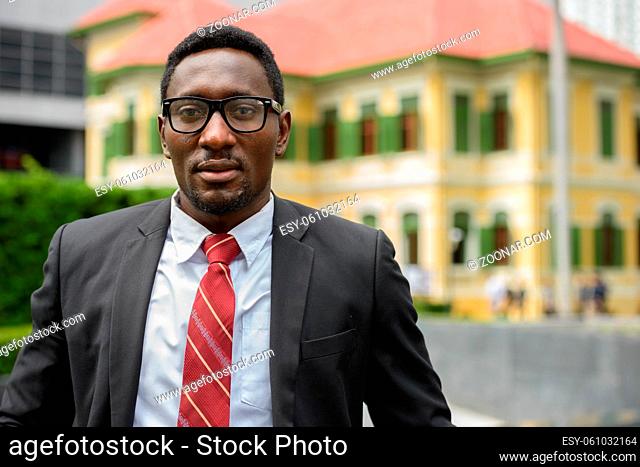 Portrait of young handsome African businessman wearing suit in the city streets outdoors