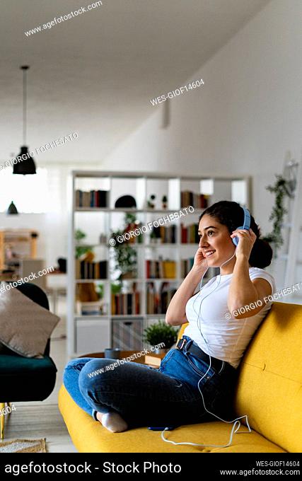 Smiling woman adjusting wired headphones at home