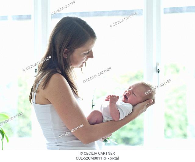Mother holding infant son by window