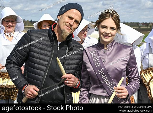 13 April 2023, Brandenburg, Beelitz: The new asparagus queen Charlotte Schmidt and TV chef Ralf Zacherl stand in a field with fresh asparagus at the start of...