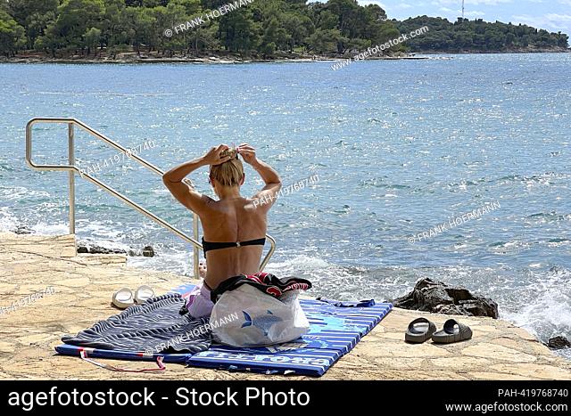 Plava Laguna, Adriatic coast near Porec / Croatia, beach. Vacationer, young woman, single, sunbathes on the stone beach, rocky beach. ?