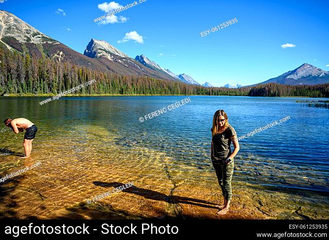 Summer scene of the Honeymoon Lake with a woman standing in the lake and enjoying the view of the surrounding mountains in the Jasper National Park, Alberta